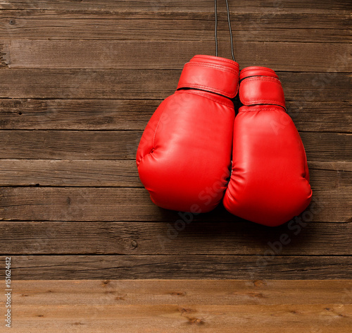 Two red boxing gloves hung on a wooden brown background, empty space © somemeans