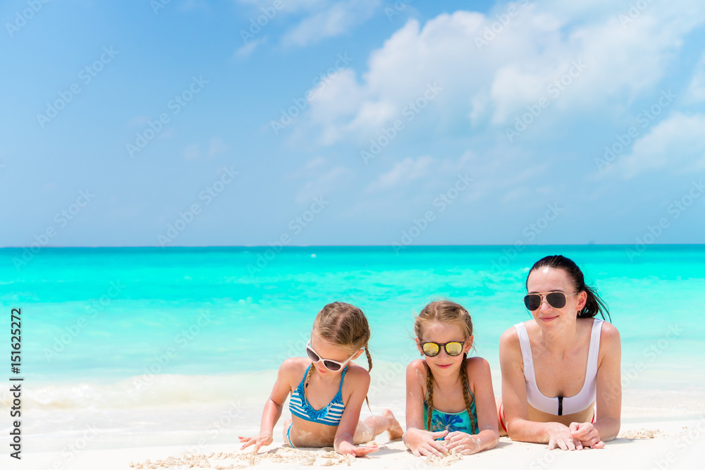 Portrait of young beautiful mother and her adorable little daughters at tropical beach