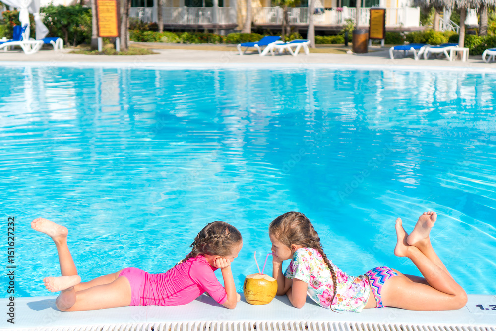 Little girls in outdoor swimming pool drink coconut milk