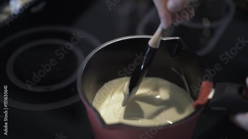 Close up of woman s hand stirring white cream in a pan at home. Locked down real time close up shot photo