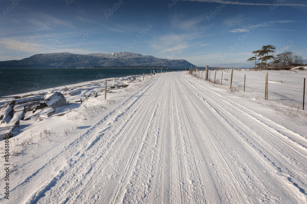 Snow Covered Country Road. Snow covers a road in the San Juan Islands of Washington State with Orcas Island in the background.