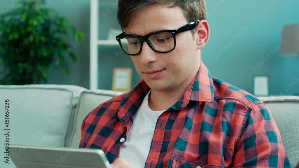 Portrait of attractive man using tablet for chating with friends, sitting on a couch at home. Portrait of attractive man using tablet for chating with friends, sitting on a couch at home.