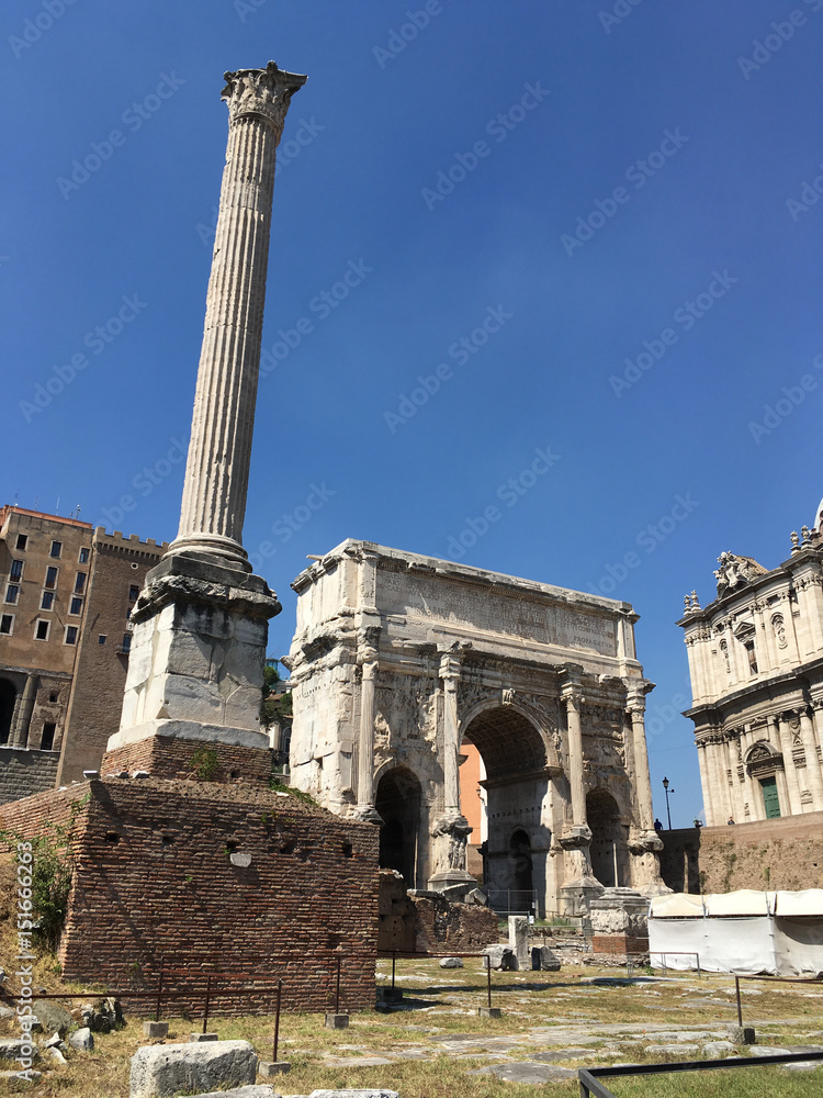 Septimius Severus Arch and the Column of Phocus on the Via Sacra in the Roman Forum in Rome, Italy on a cloudless, hot summer's day.  Dark blue sky.