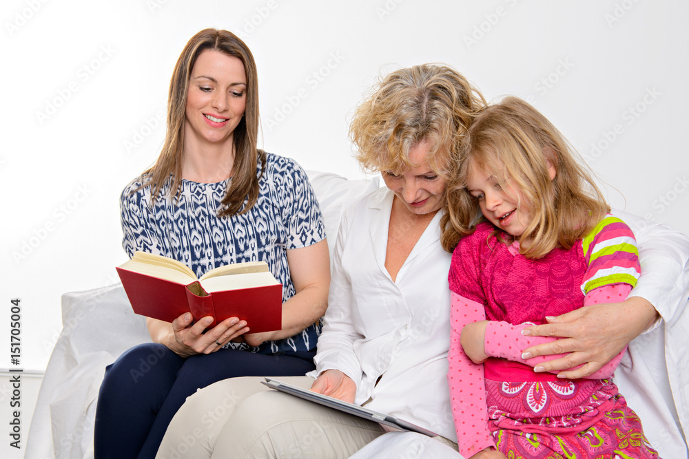 woman with daughter and grandchild together reading in book and tablet PC woman with daughter and grandchild together reading in book and tablet PC