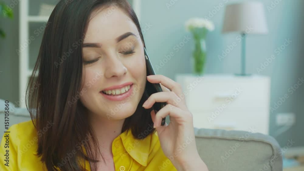 Attractive young woman talking on smart phone while relaxing on couch in the living room. Attractive young woman talking on smart phone while relaxing on couch in the living room.