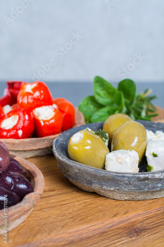 Mediterranean appetizer antipasti tapas bowls with green and calamata olives, feta cheese, stuffed pepper, herbs on wooden plank