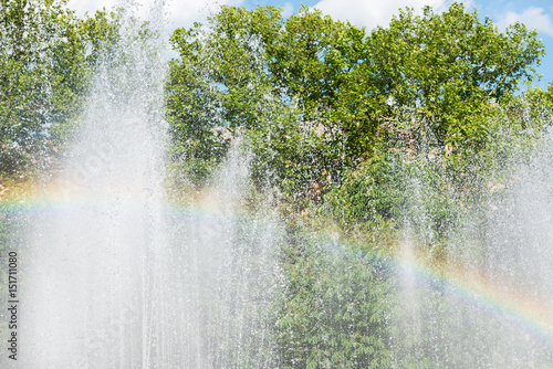 rainbow over water in fountain with green trees on background
