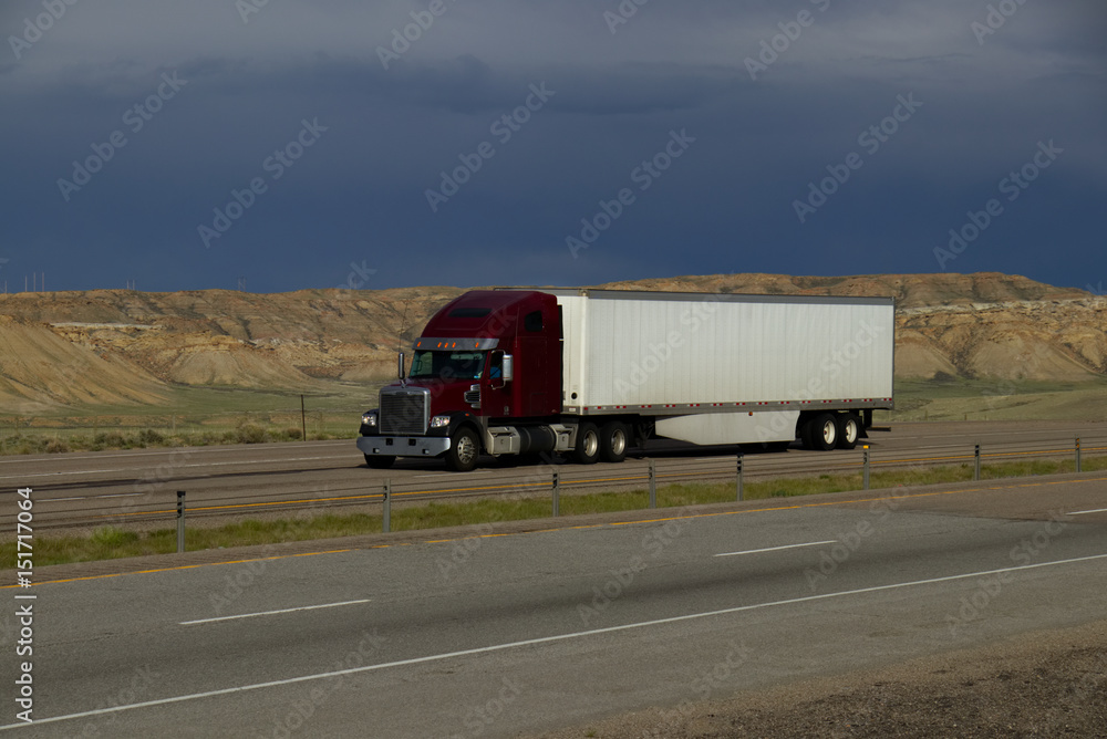 A dark red or Maroon freightliner semi tractor pulls a white trailer down rural Interstate 80 in Wyoming on May 4th, 2017,