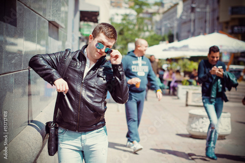 Tableau sur toile Young man townspeople in black jacket walking around the European city, drinking