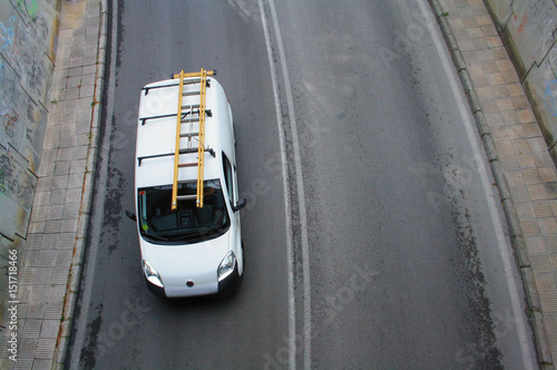 a van with a ladder on the roof going down the road