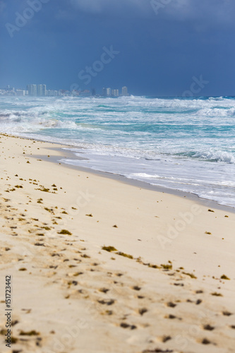 Beach view. Very long sand beach on the shores of the Caribbean sea. Sunny day, no people. City buildings on the background. 