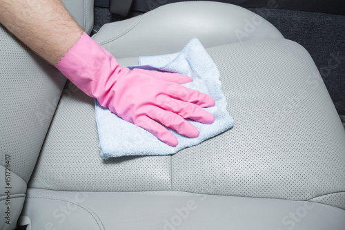 Hand in rubber protective glove with cloth cleaning a car interior's leather seats. Early spring professionally chemical cleaning or regular clean up.