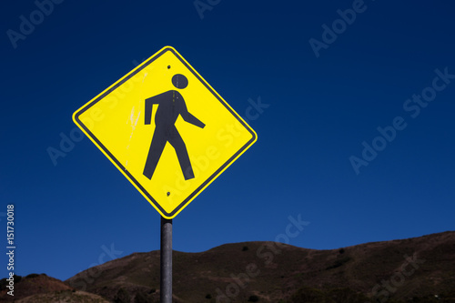 Yellow pedestrian caution sign at crossing way and intersection with blue sky background for safety transportation and people in the city