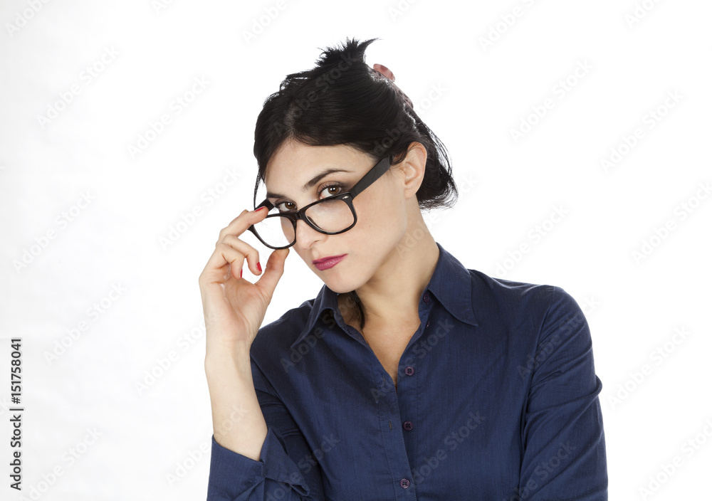 An adult (early 30s) black haired caucasian woman wearing a blue buttoned shirt, glowering her glasses and lancing at the camera with a serious expression. Isolated on white background. An adult (early 30s) black haired caucasian woman wearing a blue buttoned shirt, glowering her glasses and lancing at the camera with a serious expression. Isolated on white background.