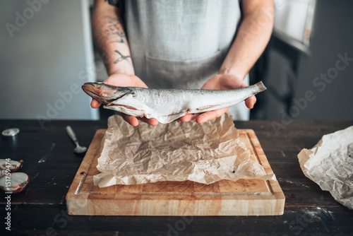 Photography Chef hands holds raw fish over cutting board