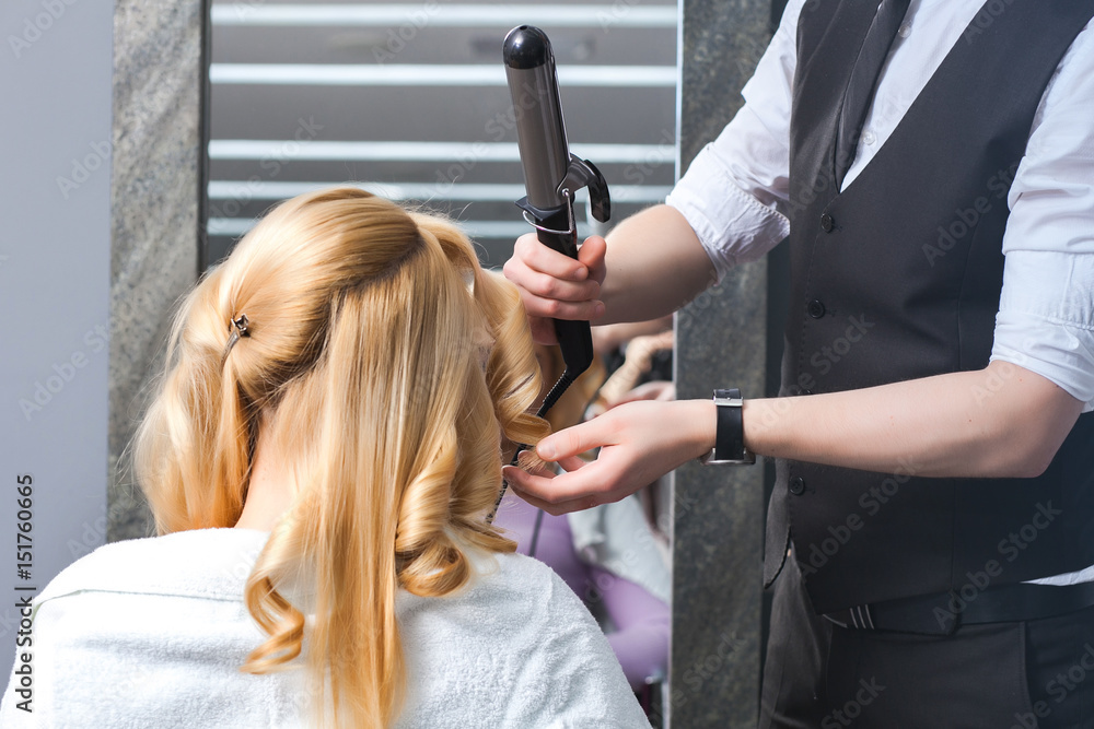 Fototapeta premium handsome Hairdresser does a hairstyle for a blonde girl in a beauty salon