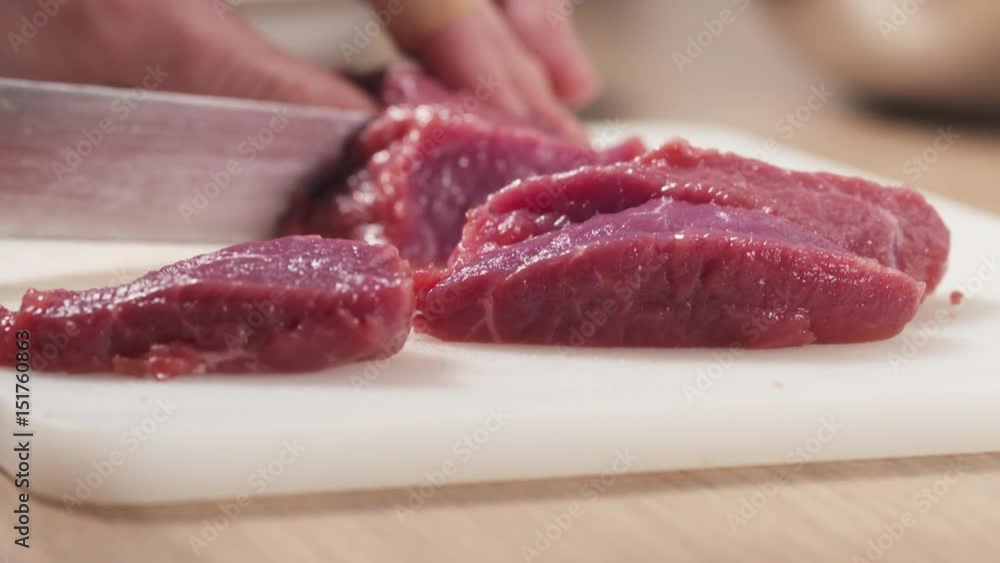 Slow motion slide shot of young female hand cutting raw beef with a knife on plastic board, 180fps prores footage Slow motion slide shot of young female hand cutting raw beef with a knife on plastic board, 180fps prores footage