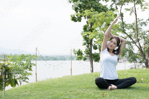 asian pregnant woman practicing yoga while listening to music on green grass in public park.  concept of prenatal exercise  maternity  fitness  healthy lifestyle and relaxation.