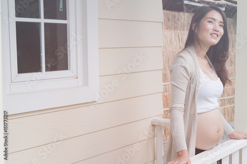 Young asian woman standing on balcony smiling with pleasure. Beautiful female expecting child having rest in front of her house