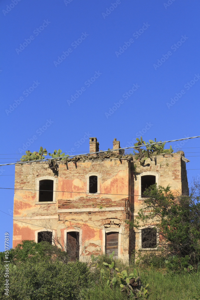 verlassenes Haus auf Sizilien in einem verwilderten Garten mit Kakteen die auf dem Dach wachsen
