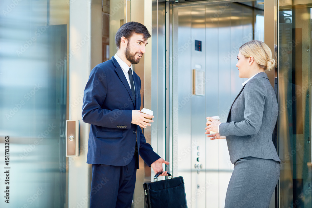 Portrait of two business colleagues dressed in formalwear meeting and talking by elevator on way to work Portrait of two business colleagues dressed in formalwear meeting and talking by elevator on way to work