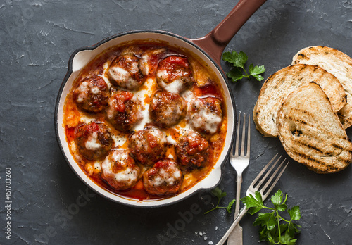 Baked meatballs with mozzarella and tomato sauce in a cast iron skillet on a dark background, top view photo