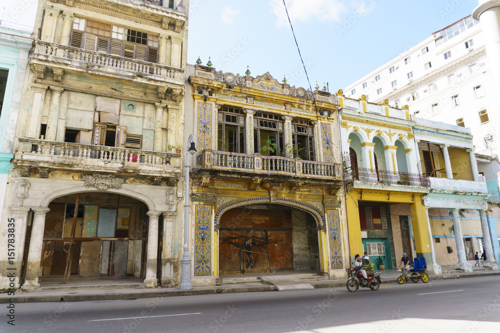 Old ancient dilapidated buildings with columns near the central road in Havana