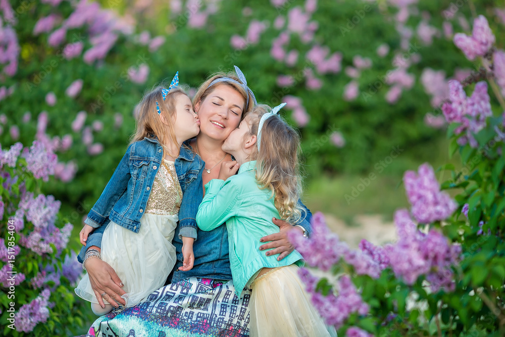 Mother woman with two cute smiling girls sisters lovely together on a lilac field bush all wearing stylish dresses and jeans coats.