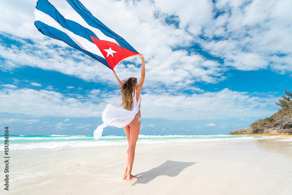 Beautiful young blond woman in white dress and bikini swimsuit is standing  a back holding the cuban flag in her arms on beach of caribbean sea foto de  Stock | Adobe Stock