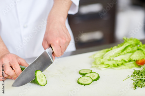 Human hand with sharp knife cutting fresh cucumber