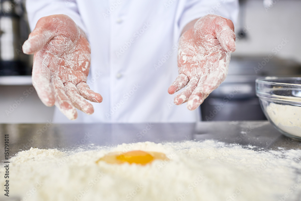 Fototapeta premium Hands of baker over workplace with pile of flour and raw yolk