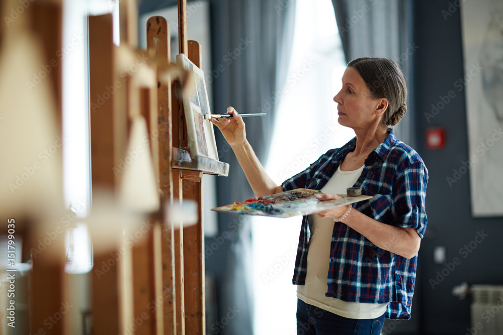 Fototapeta premium Portrait of elegant mature woman painting oil picture with inspiration in art studio