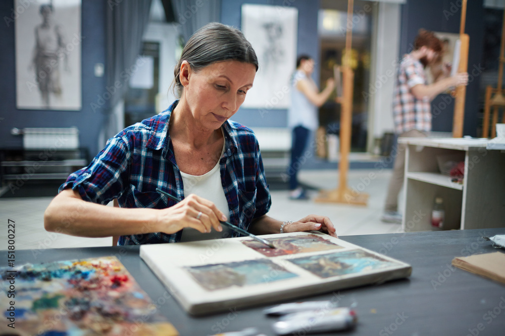 Naklejka premium Portrait of mature student working in art studio painting pictures looking focused and concentrated