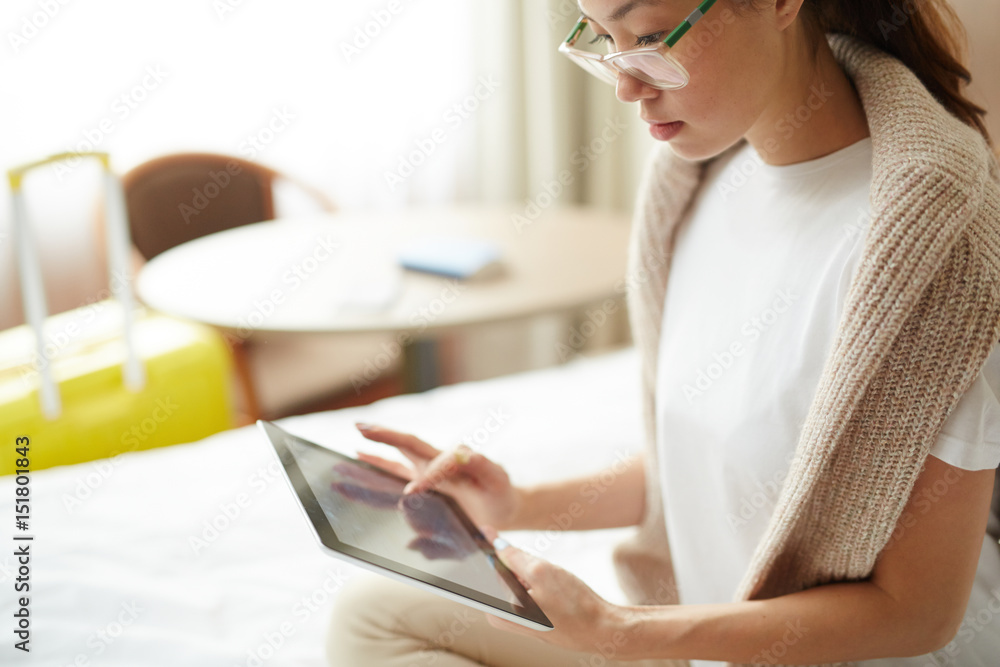Portrait of young Asian woman using modern digital tablet sitting on big bed in hotel room, looking for city map and food ordering Portrait of young Asian woman using modern digital tablet sitting on big bed in hotel room, looking for city map and food ordering