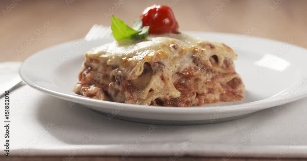 Slide shot of homemade lasagna portion on white plate on wood table, 4k prores footage Slide shot of homemade lasagna portion on white plate on wood table, 4k prores footage