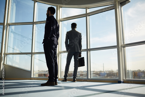 Two businessmen in suits standing inside office center