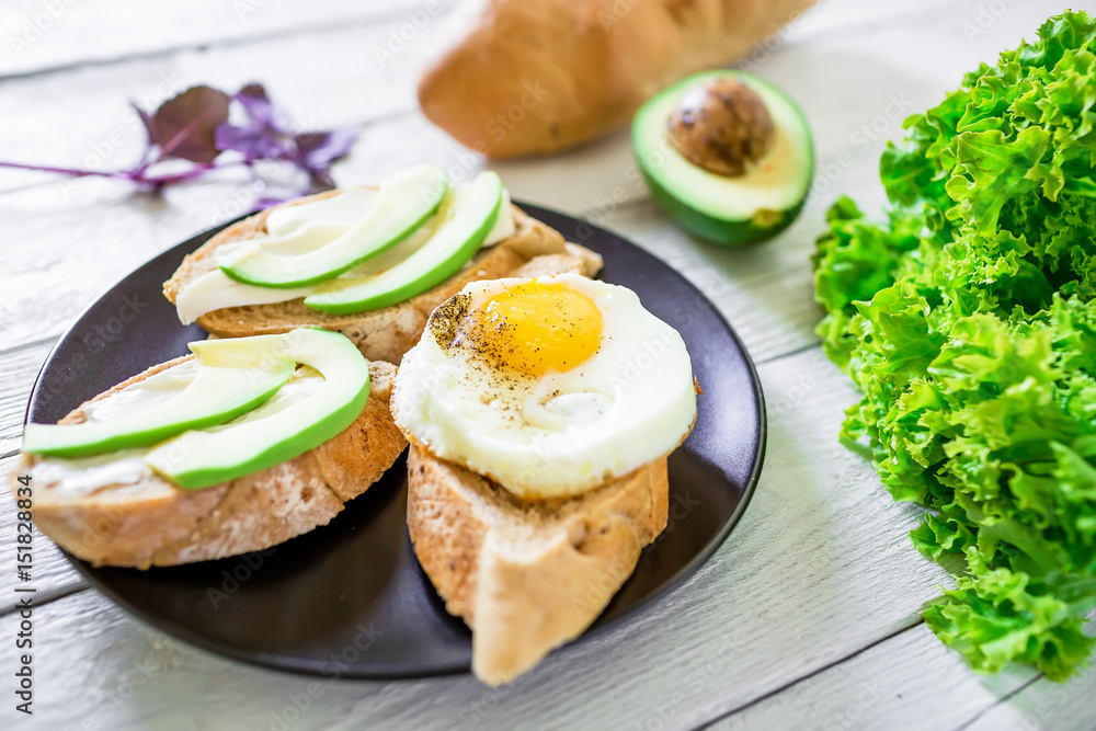 Tasty sandwiches with avocado and egg on a dark plate on wooden background