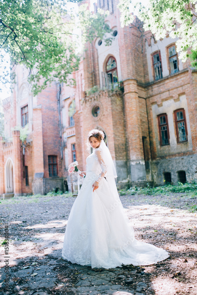 Very beautiful bride with her delicate bouquet posing near the castle