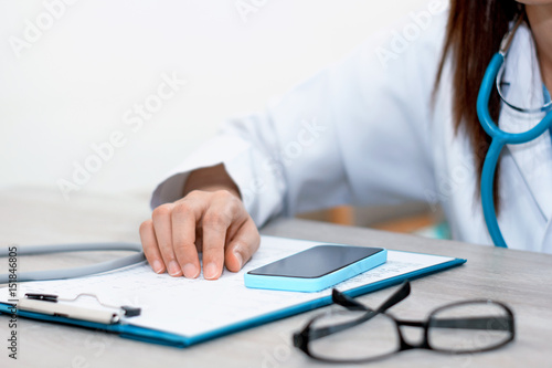 Close-up of a female doctor in office filling out application form with smartphone , sitting at the table in the hospital