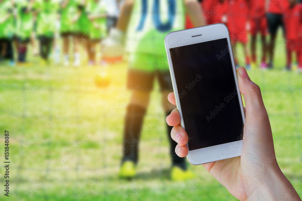 hand holding smartphone with young boy as a soccer goalkeeper during football match ready to save.