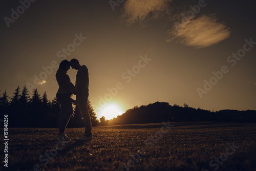 Couple expecting a child holding hands facing each other at sunset.
