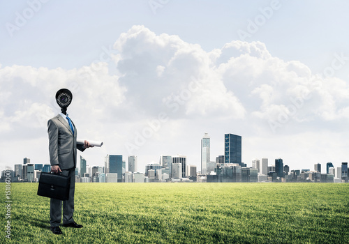 Camera headed man standing on green grass against modern citysca