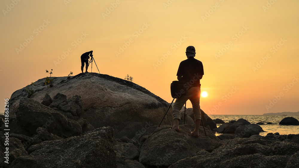 silhouette photographer on sunrise on the rocks by the sea