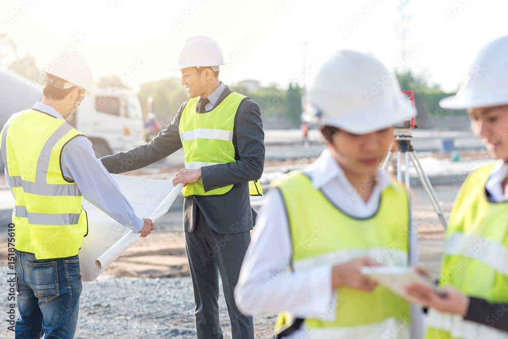 Engineer and builder review blueprint during team meeting at construction site in the morning with sunlight Engineer and builder review blueprint during team meeting at construction site in the morning with sunlight