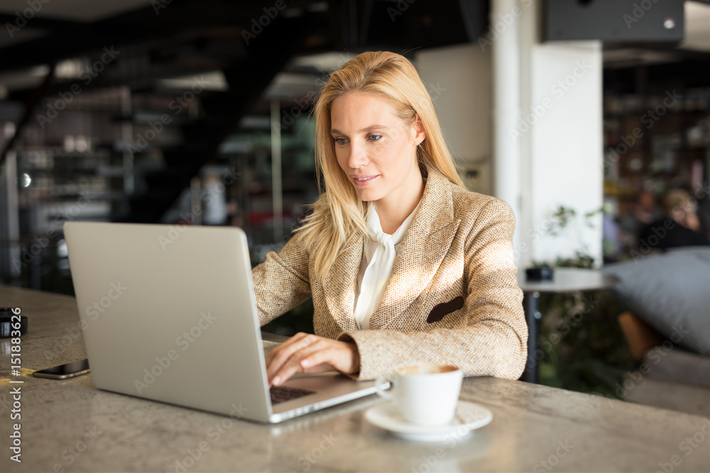 Fototapeta premium Modern business woman in city cafe. Drinking coffee and surfing the web.