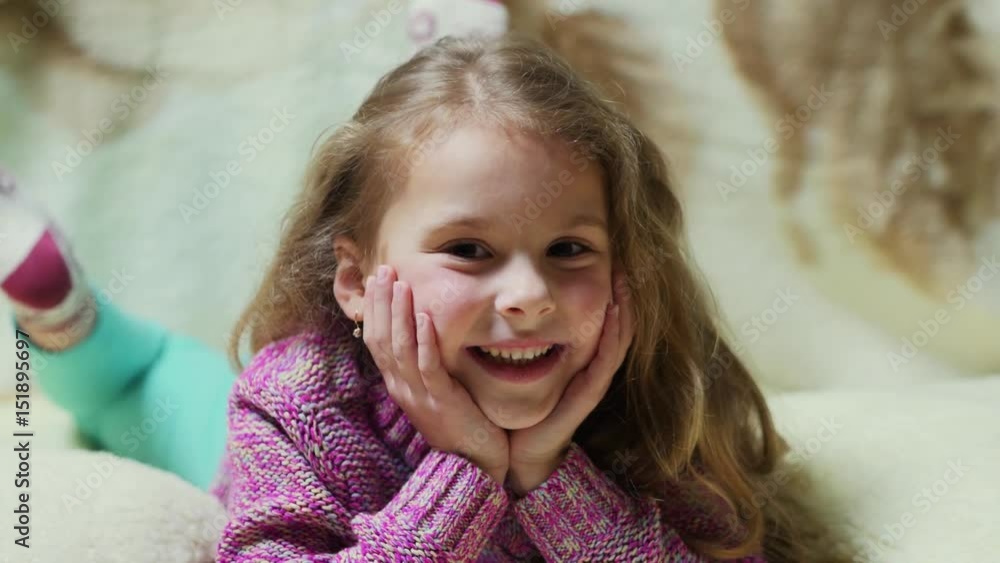 Beautiful little girl smiling at camera. Portrait of cheerful kid lying on couch Beautiful little girl smiling at camera. Portrait of cheerful kid lying on couch