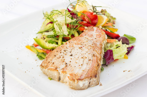 Tuna steak with colorful vegetables served in a restaurant, white background.