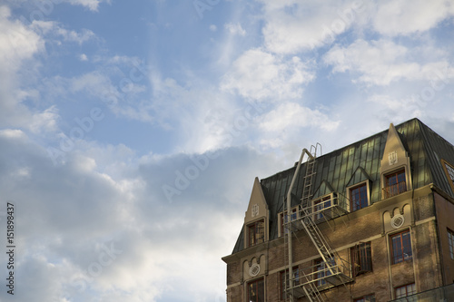 Dramatic Upward Skyward View, Tall Victorian City Apartment Building, Green Mansard Roof, Brick Front, Red Trim Windows, Fire Escape/Stairs, Blue Sky White Clouds, Daytime - West Coast, USA © Jacquie Klose