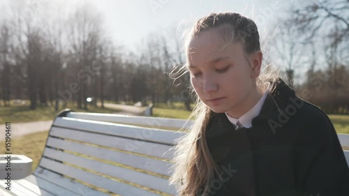 Gimbal fly around shot of female teen girl using smartphone sitting on bench in spring sunny day, uhd prores footage photo