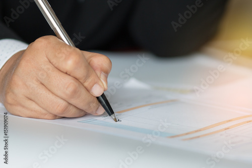 Hand holding pen for signing in financial data and counting on document chart, business concept, close-up